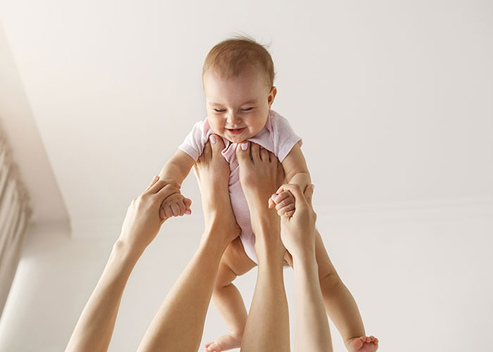 Baby lifted in the air, smiling joyfully, held by adult hands, expressing happiness and innocence.