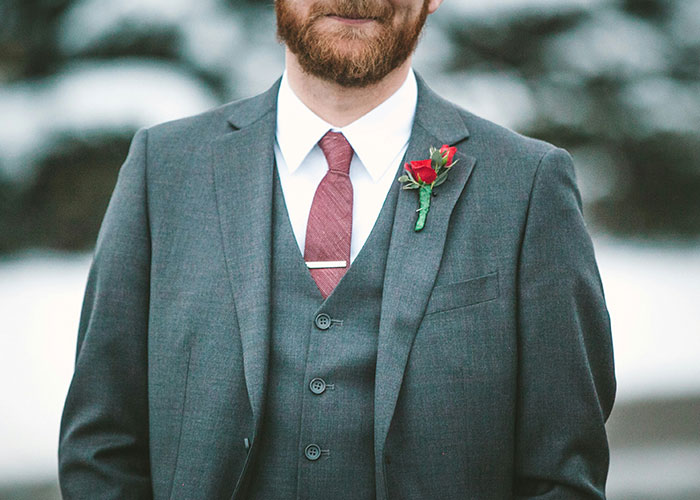 Man in gray suit with red tie and boutonniere, related to secrets spilled by drunk people.