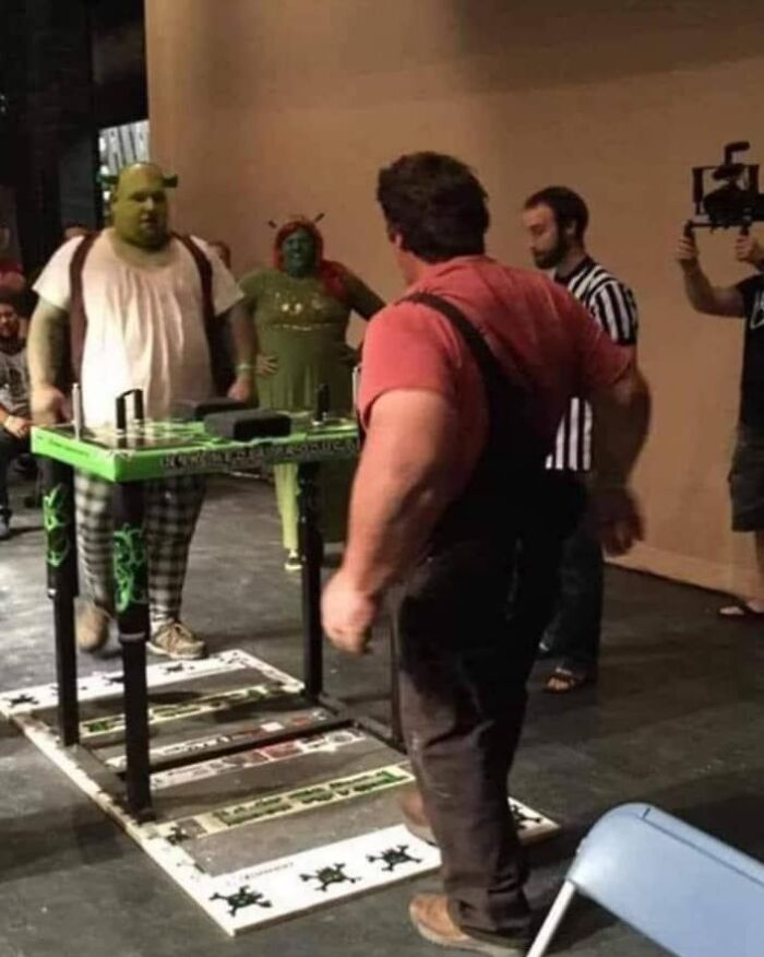 People dressed in green costumes at a table, resembling a quirky album cover scene.