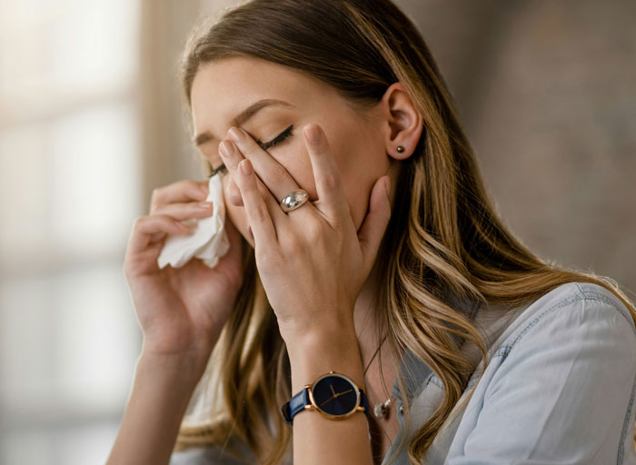 Woman crying into tissue, upset about brother-in-law&rsquo;s drunken behavior, wearing a watch and casual clothing.