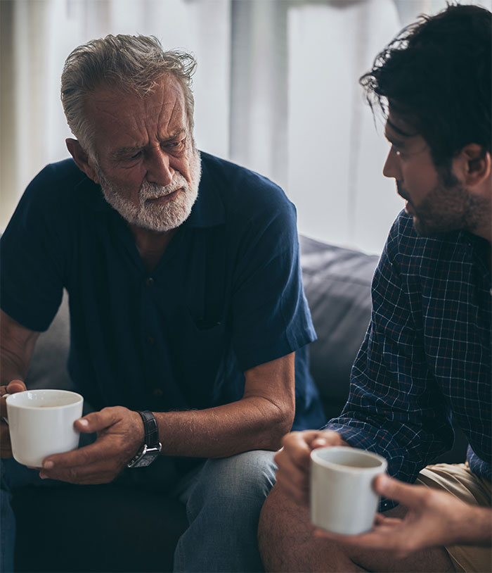 Two men having a serious conversation over coffee about family and ex-partner holiday plans.