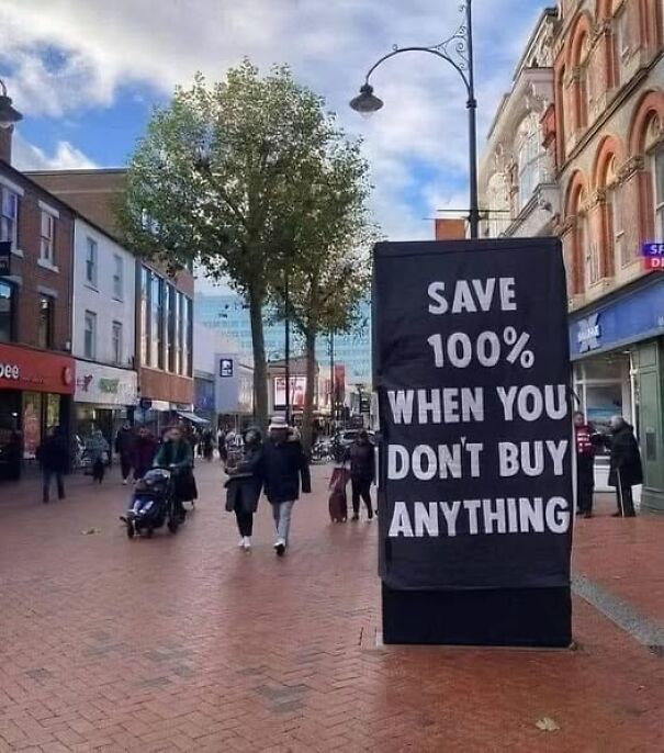 Weird and absurd sign on a busy street reading "Save 100% when you don't buy anything."