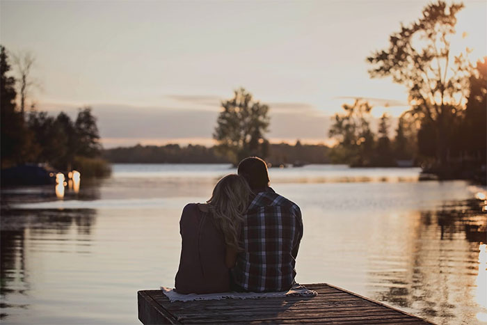 A couple sitting on a dock at sunset by a lake, evoking emotions tied to family and relationship dynamics.
