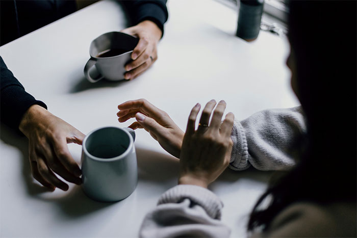 Hands holding mugs over a table, discussing wedding dress preferences for comfort.