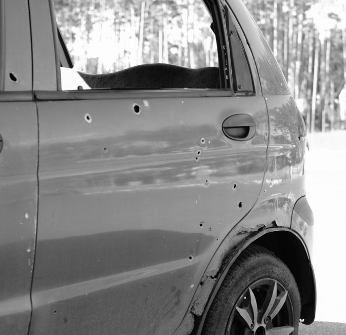 Car with bullet holes on the side, parked in a wooded area, illustrating surprising speeding reasons shared with officers.