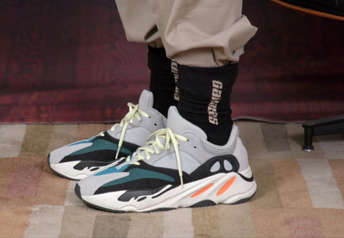 Person wearing trendy sneakers with black socks and beige pants standing on a patterned rug.