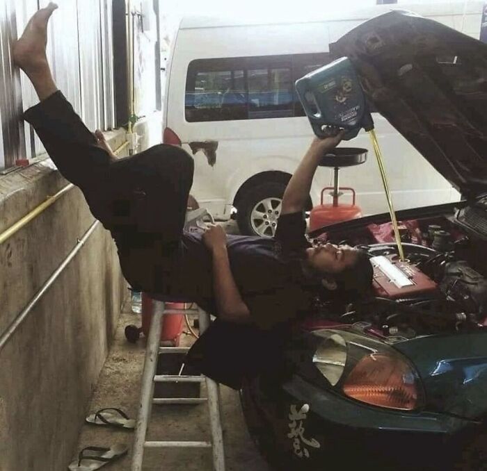 Man in an unusual position, pouring oil into a car engine, resembling a weird photo for a potential album cover.