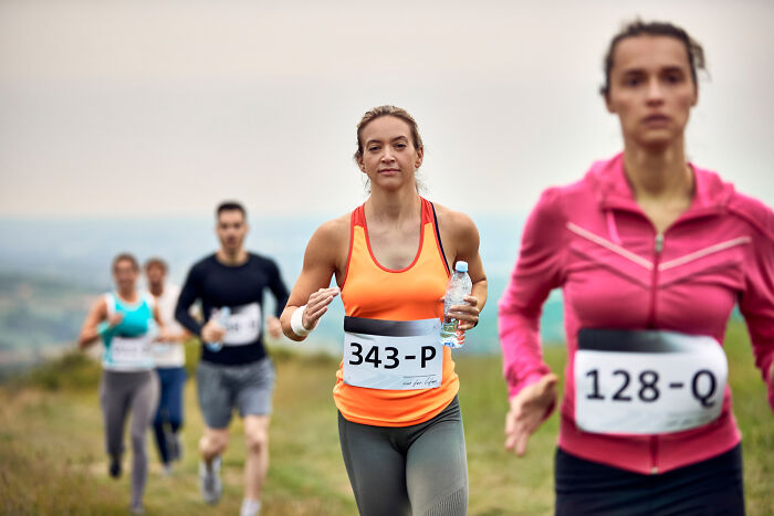 Runners in a race on a trail, wearing numbered bibs, with one holding a water bottle.