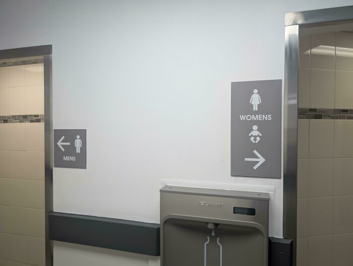 Restroom signs for men and women with a baby changing station below in a clean public bathroom space.
