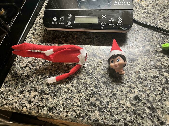 Elf doll head detached from body on kitchen counter near induction cooktop, showcasing funny dads doing their best humor.