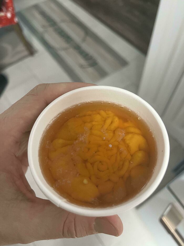 Unusual dish in a cup with orange, brain-like contents held in hand, showcasing a bizarre culinary creation.