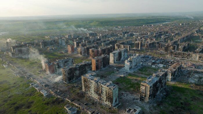 Aerial view of urban hellscape with damaged buildings and smoke rising.