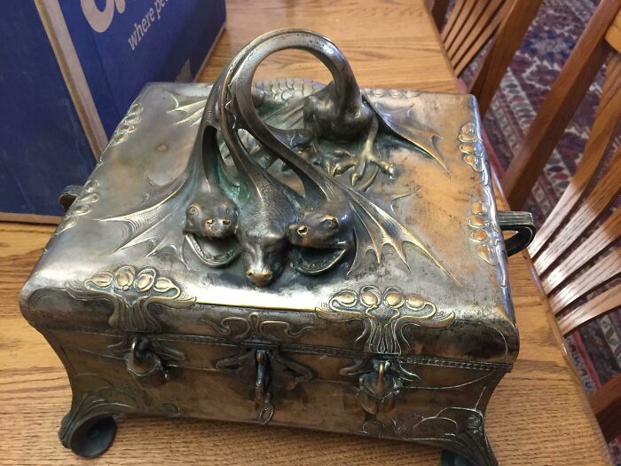 Ornate antique silver box with three dragon heads on the lid, a unique cool inheritance item on a wooden table.