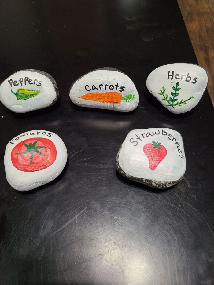 Painted garden rocks labeled as peppers, carrots, herbs, tomatoes, and strawberries, a thoughtful gift idea.