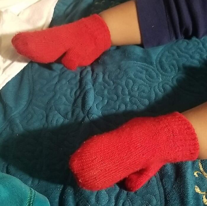 Child wearing red mittens on their feet, lying on a blue quilt.