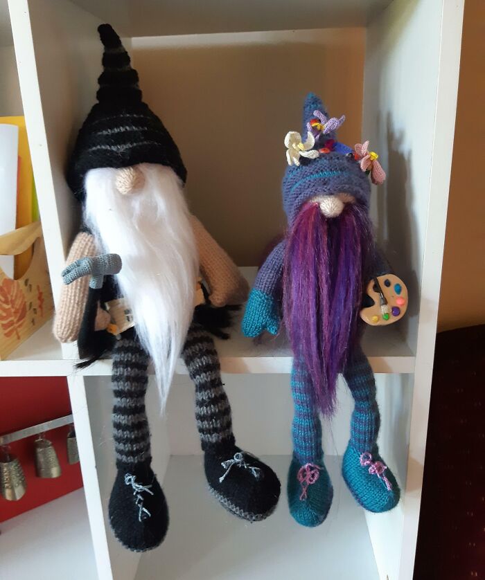 Knitted gnome dolls on a shelf, one holding a tool and the other with a paint palette, embodying amazing mothers-in-law creativity.