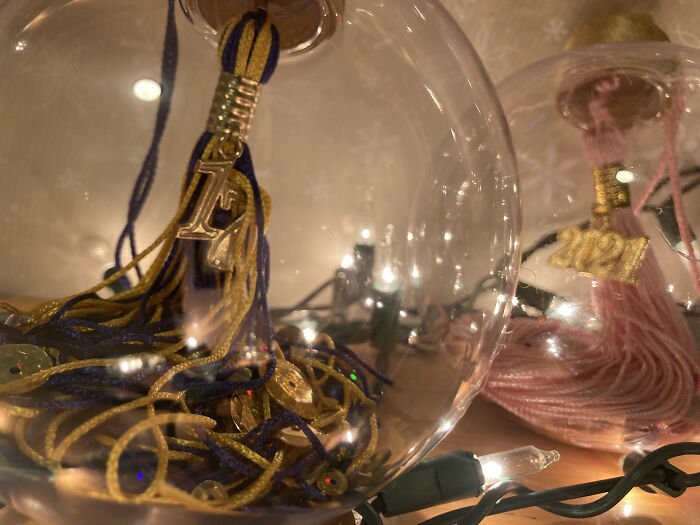 Handmade Christmas ornament with colorful tassels inside, lit by festive string lights.