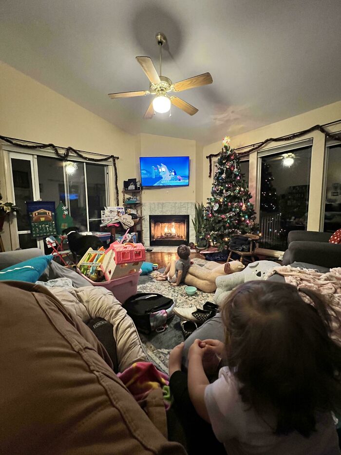 Cozy living room with kids watching TV by a Christmas tree and a fireplace, capturing wholesome dads doing their best moments.