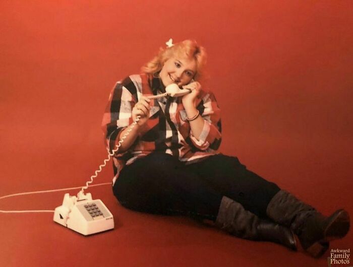 Woman sitting on red floor with an old telephone, an example of awkward family photo style.