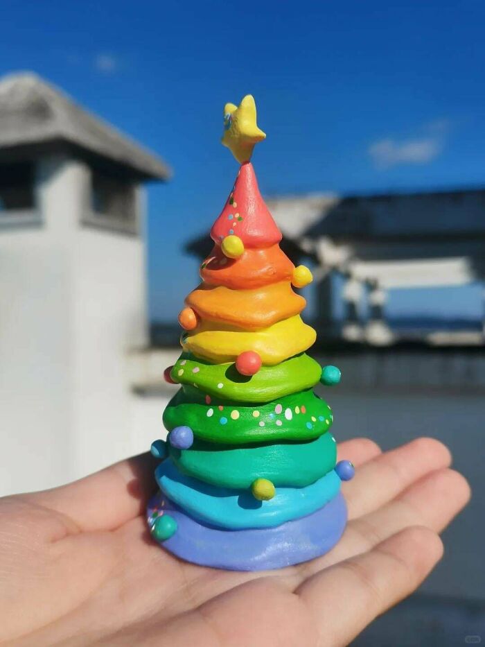 Hand holding a colorful, clay DIY Christmas tree with a star on top against a blue sky background.