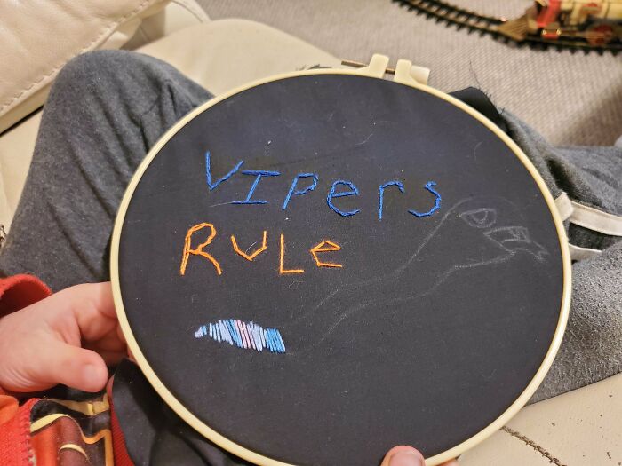 Embroidery design in progress with colorful stitched letters on black fabric held by hands on a lap.