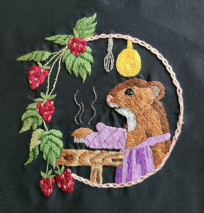 Creative embroidery of a chipmunk baking with raspberries and kitchen utensils on black fabric.