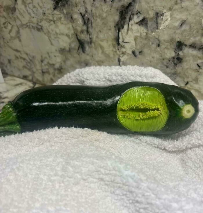 Zucchini with a peculiar marking resembling a mouth, placed on a white towel, highlighting nature's terrifying creations.