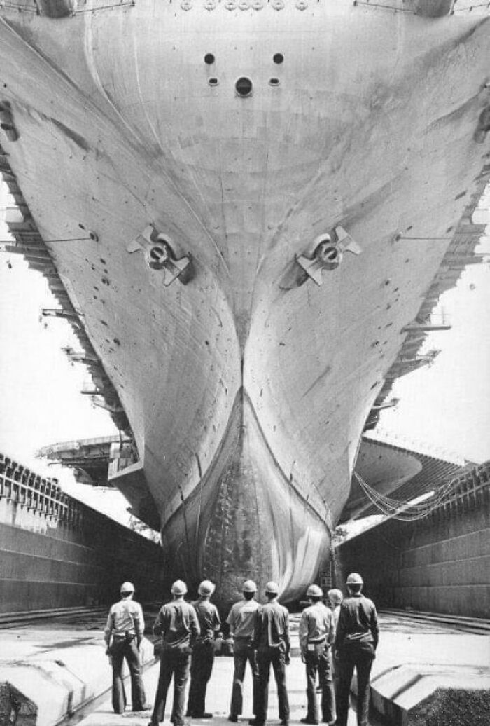 Workers standing beneath the massive hull of a battleship, showcasing an impressive example of megalophobia and scarily big structures.