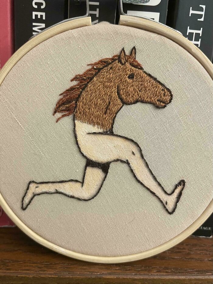 Embroidery design of a horse head on a human body running, stitched on a beige fabric in an embroidery hoop.
