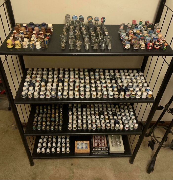 Unique collections of decorative thimbles displayed on black shelves.
