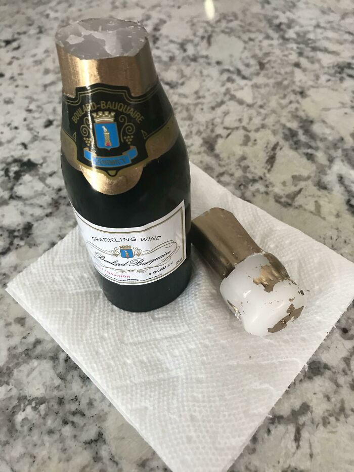 Miniature sparkling wine, a disappointing gift on a paper towel, showcasing the label and detached cork on a granite surface.