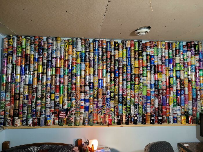 Wall of colorful soda cans forming an unexpected unique collection in a room setting.
