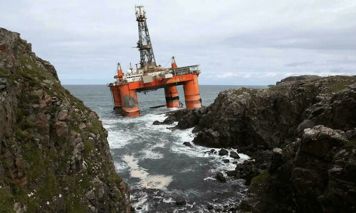 Large offshore oil rig towering between rocky cliffs over rough ocean waters, showcasing impressive scale for megalophobia.