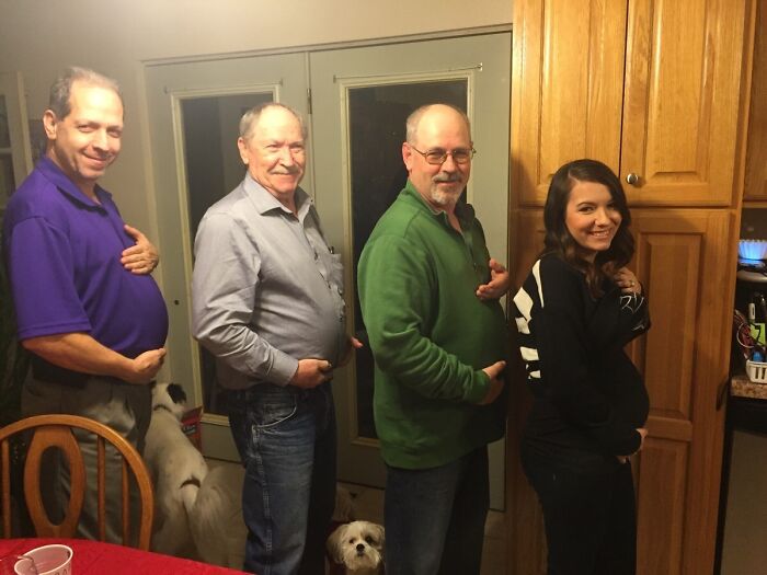 Group imitating pregnant belly poses, showcasing funny pregnancy situations in a lighthearted indoor setting.