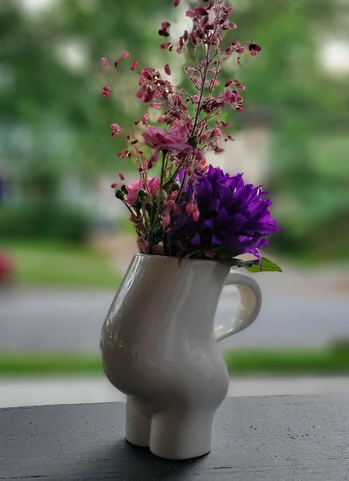 Quirky vase with flowers in a humorous design on a blurred outdoor background.