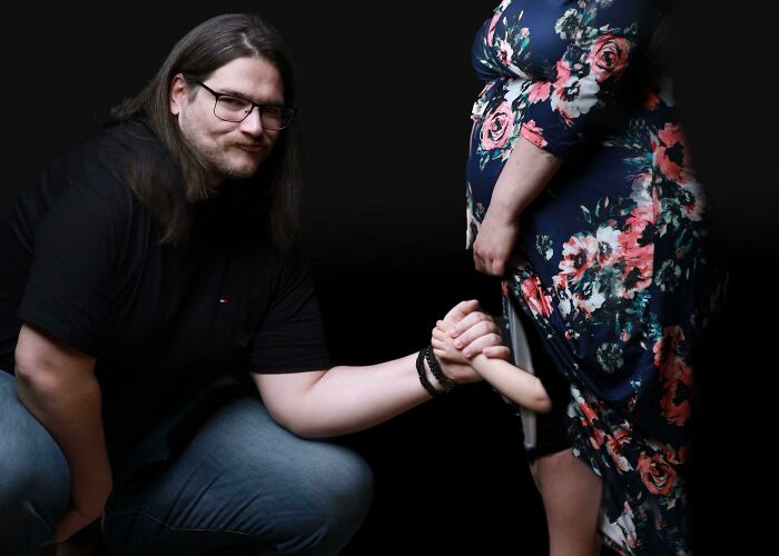 Man holding a fake baby hand emerging from a floral dress in a humorous pregnancy situation.