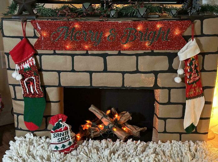 DIY Christmas decorations on a cardboard fireplace with stockings and a "Merry & Bright" sign.