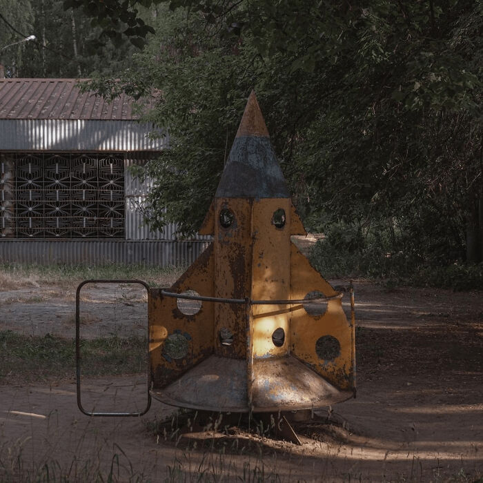 Rusty yellow rocket playground equipment, exemplifying urban hell amid overgrown vegetation and decaying structures.