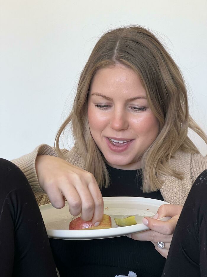 Pregnant woman amusingly eating apple slices, illustrating funny pregnancy situations.