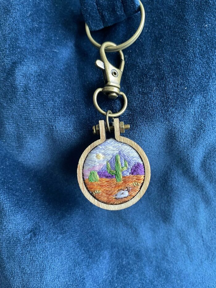 Small embroidery design keychain featuring a desert scene with cactus and mountains on a blue fabric background.