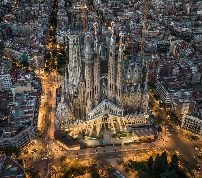 Aerial view of an impressive architectural feat, the illuminated Sagrada Familia amidst a cityscape at dusk.