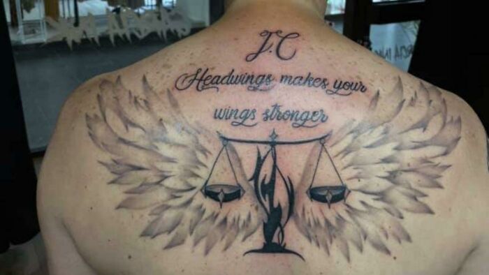 Back tattoo fail with misspelled quote, scales, and wings.