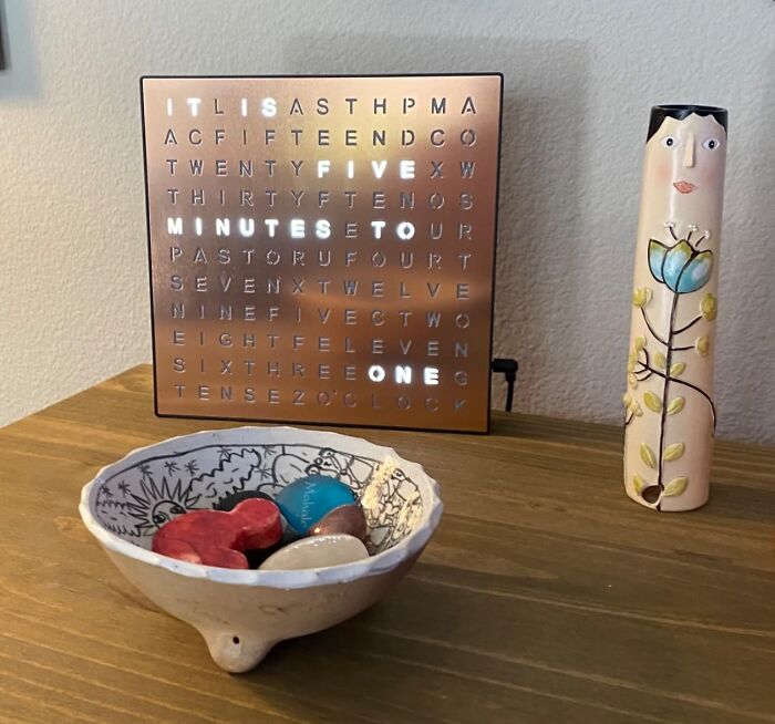 Unique gifts for women: a word clock, a decorative vase, and colorful stones in a ceramic bowl on a wooden table.
