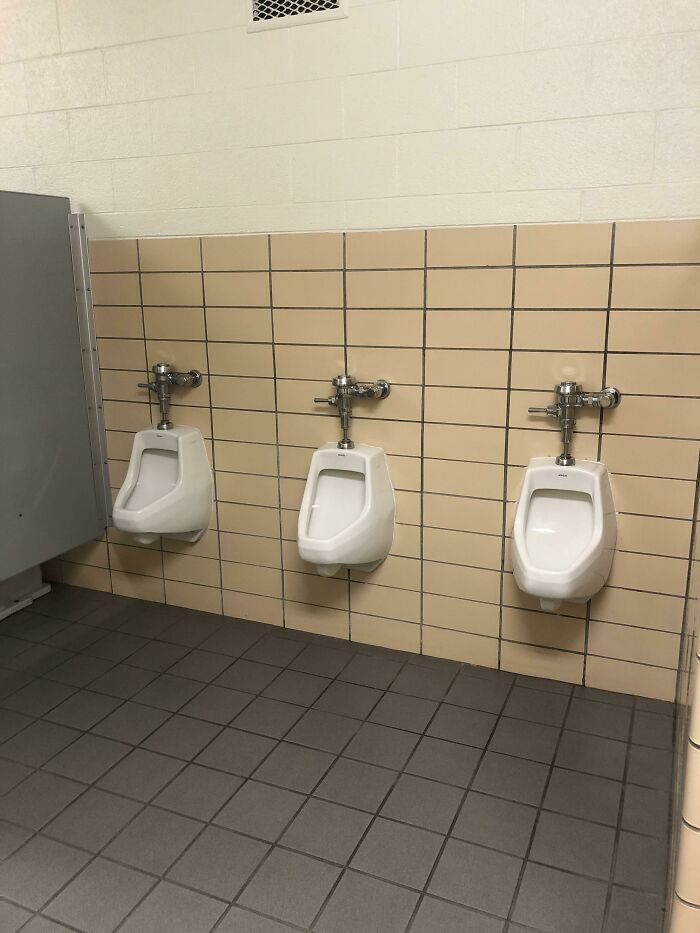 Three urinals in a school bathroom setting, reflecting common student experiences.
