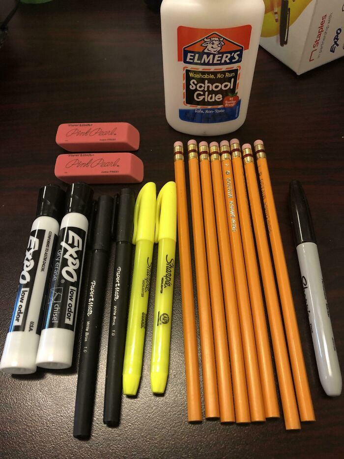 School supplies including pencils, erasers, markers, glue, and highlighters arranged on a desk for a school setting.