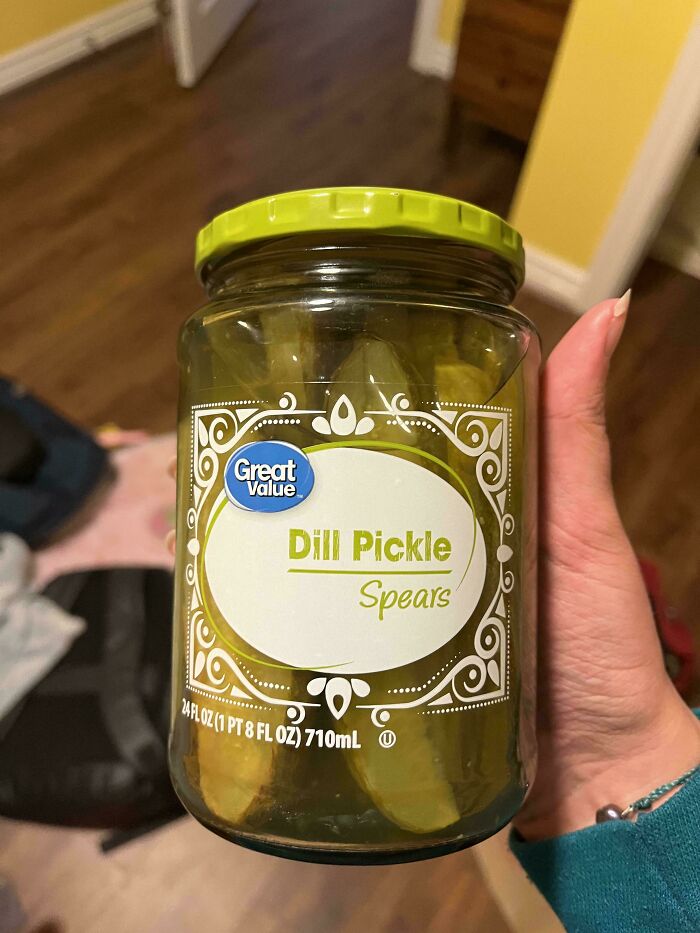 A hand holding a jar of dill pickle spears, a disappointing presents gift in a kitchen setting.