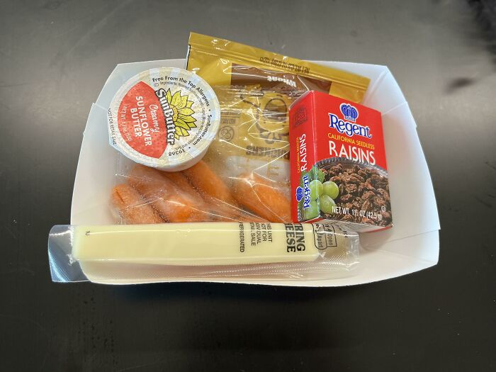 School lunch with sunflower butter, raisins, carrots, and string cheese on a tray.