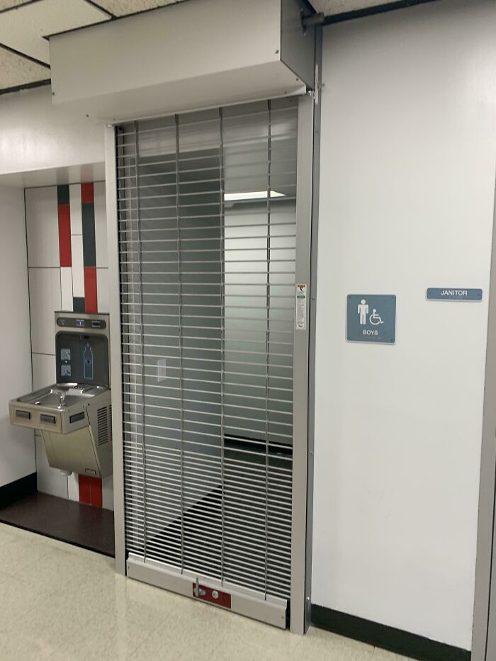 Closed school restroom with metal gate, next to a water fountain.