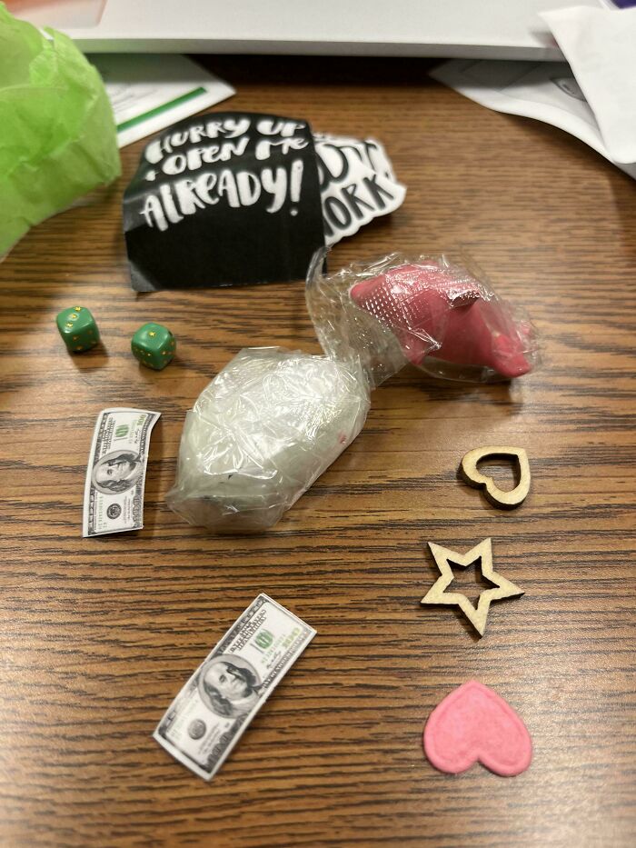 Disappointing gifts on a wooden table: dice, faux cash, and decorative shapes with a playful note.