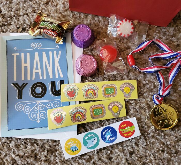 Thank you card with disappointing gifts: candy, stickers, and medal on carpet.